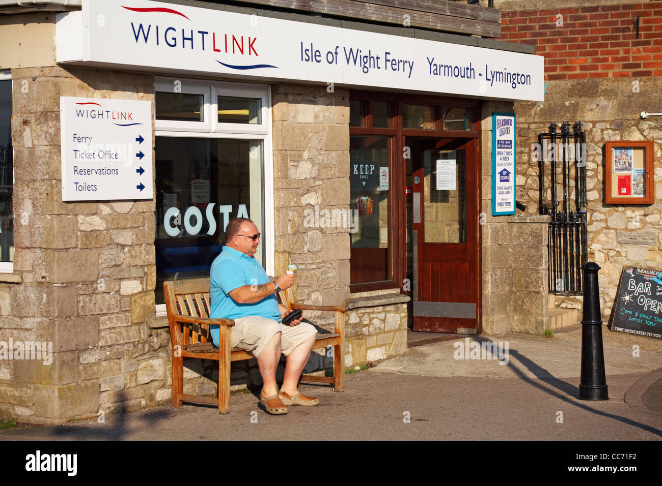 Mature man sat on bench enjoying an ice cream outside Wightlink ferry office at Yarmouth, Isle of Wight, Hampshire UK in September Stock Photo