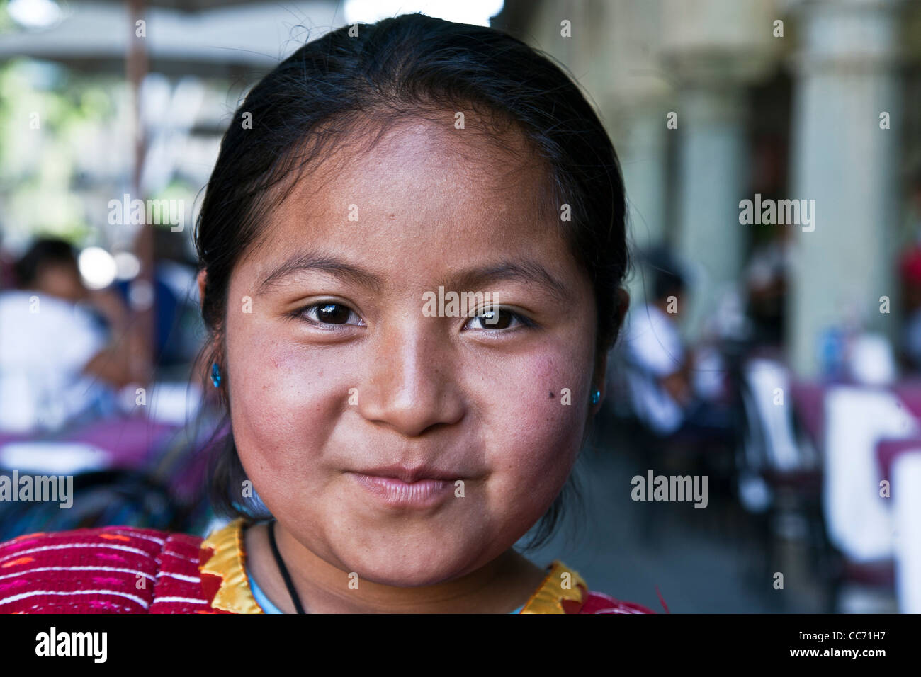 mischievous  young Triqui Indian girl vendor consents to a photo in loggia of restaurant area of Oaxaca Zocalo Stock Photo
