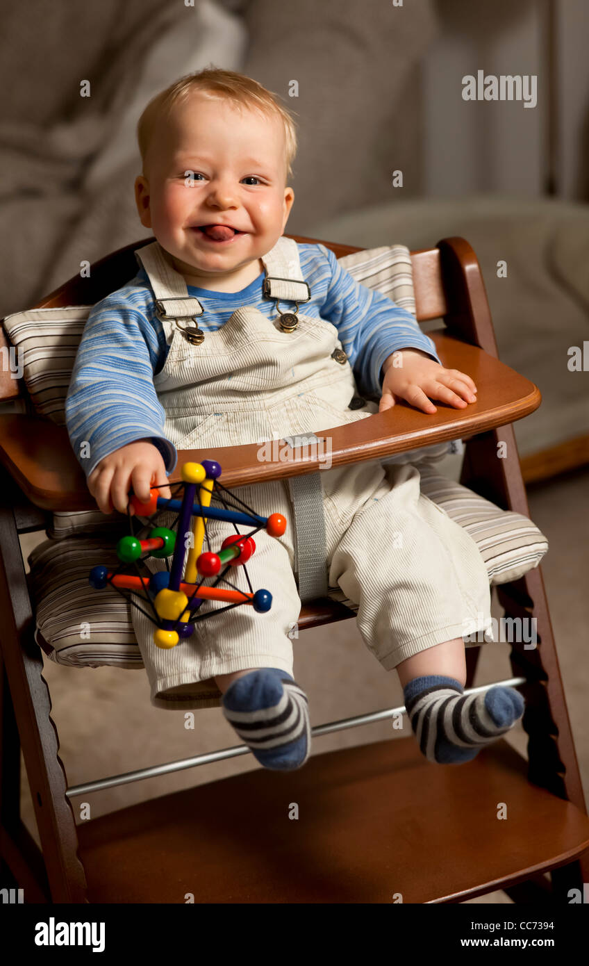 Happy young boy (10 months old) in a highchair with a toy, smiling Stock Photo