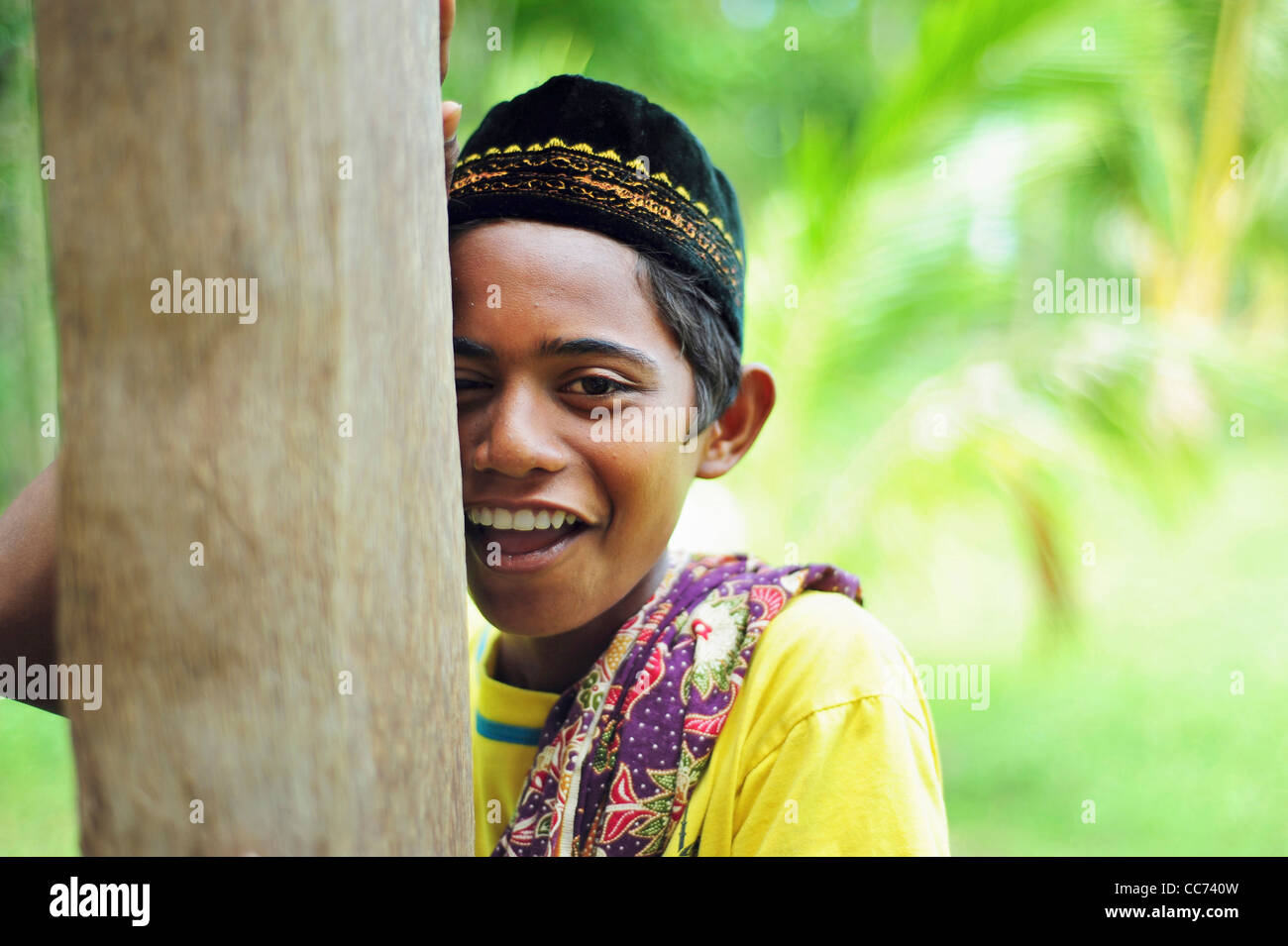 Indonesia, Sumatra, Banda Aceh, young boy in traditional dress smiling and hiding behind tree Stock Photo