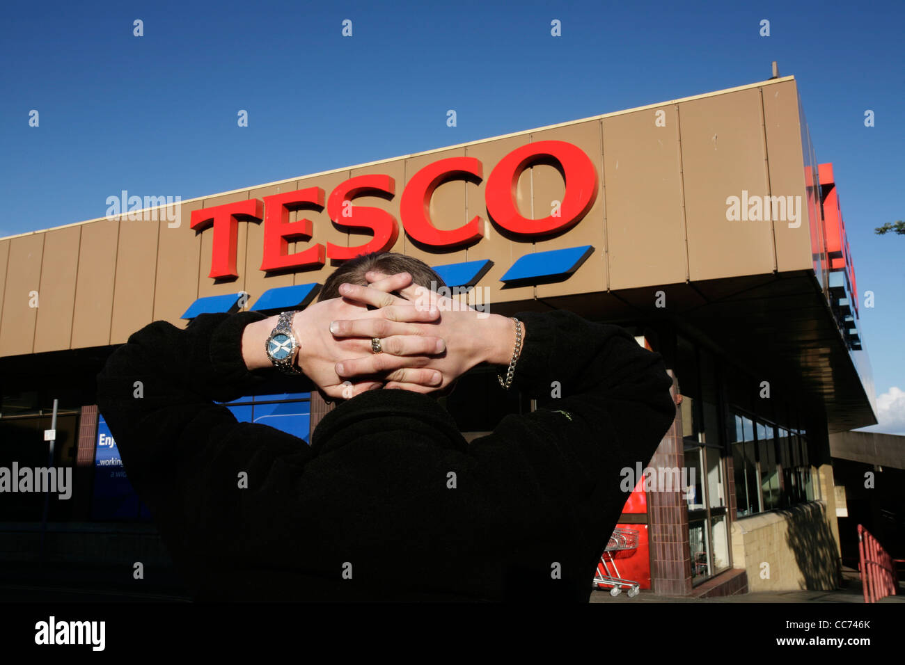 A man holds his hands behind his head in front of a Tesco supermarket Stock Photo