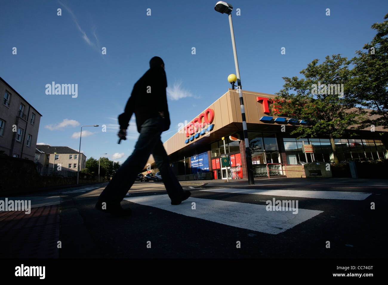 A man walks across a pedestrian crossing towards a Tesco supermarket Stock Photo
