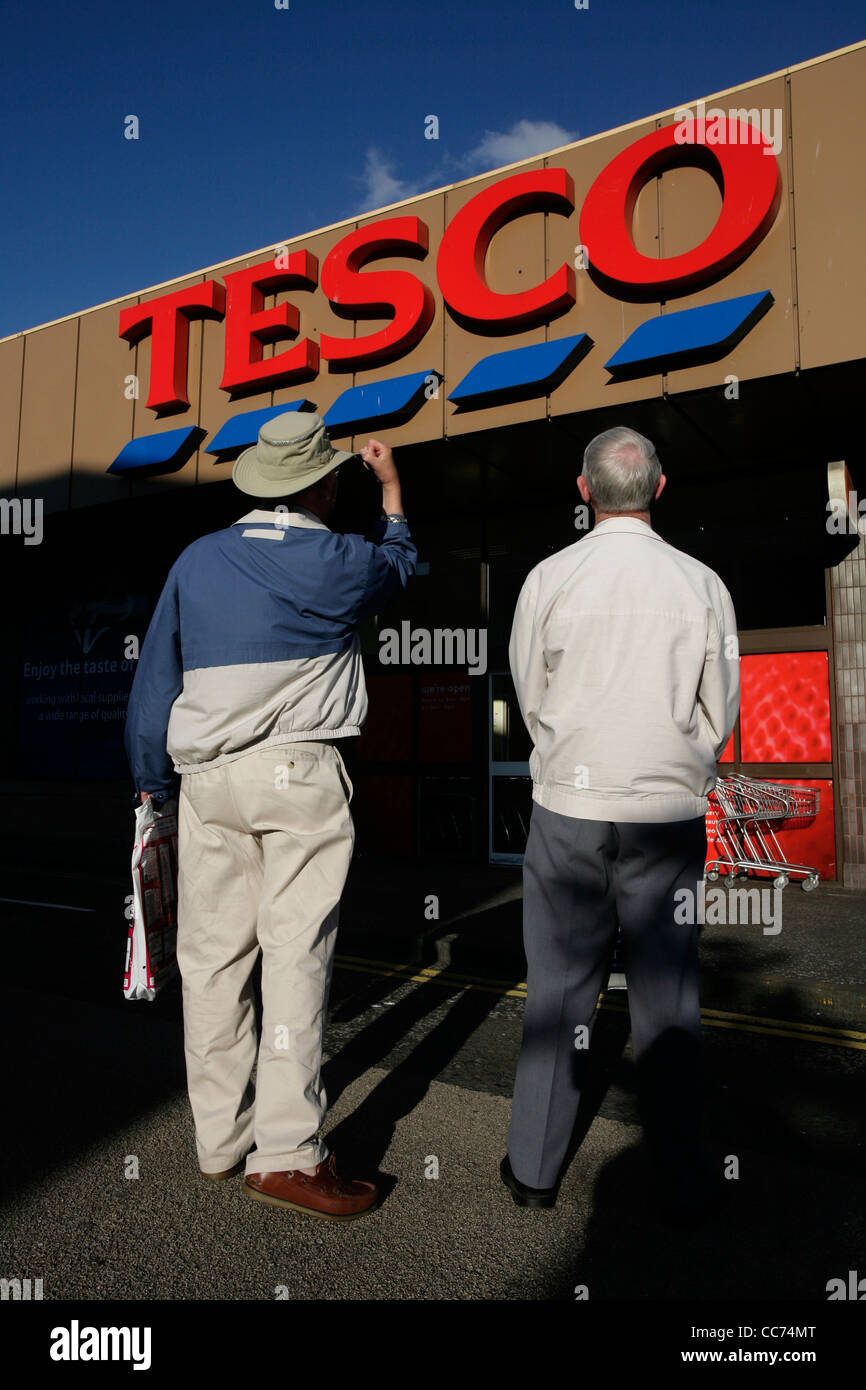 Two elderly men standing outside a Tesco supermarket, one shaking his fist towards the store Stock Photo