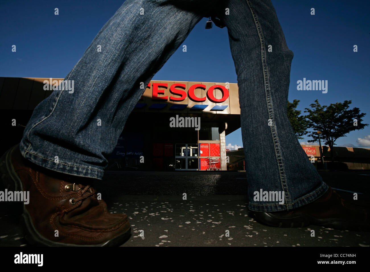 A Tesco store seen through the legs of someone walking past Stock Photo