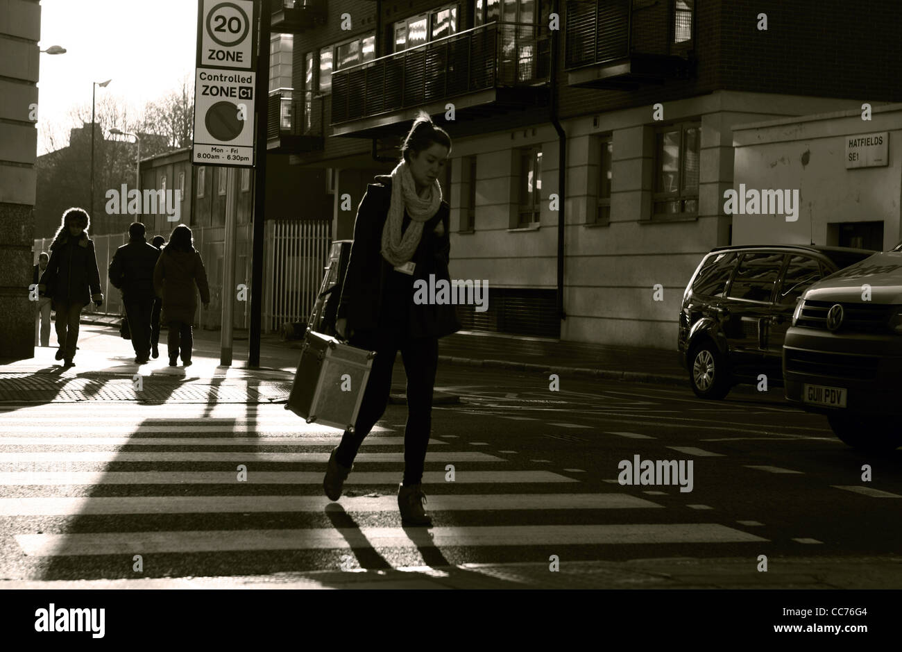 a female walks across a zebra crossing in London while a vehicle waits and people walk in the background, photographed in sepia Stock Photo