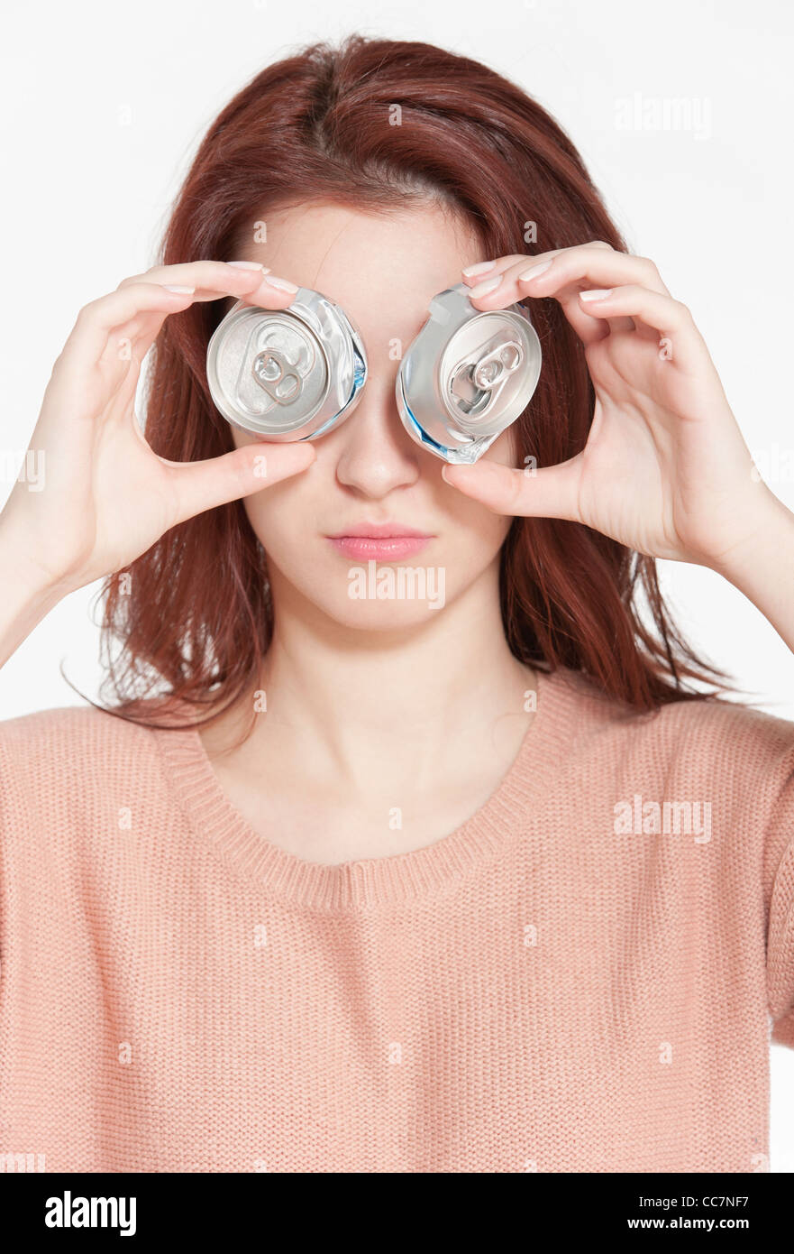 Young woman holding two crushed drink cans in front of face Stock Photo