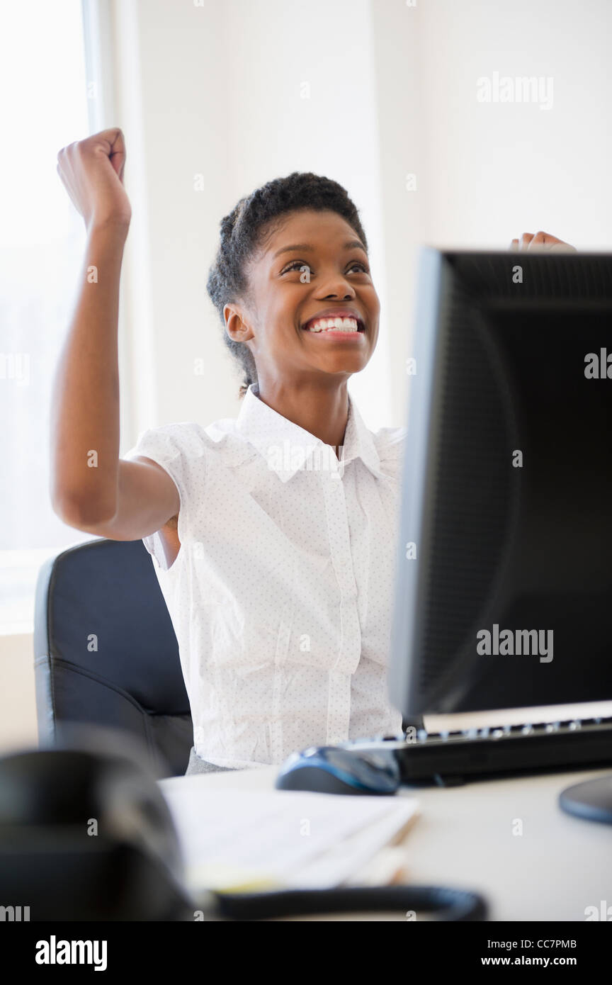 Excited Black businesswoman cheering at desk Stock Photo