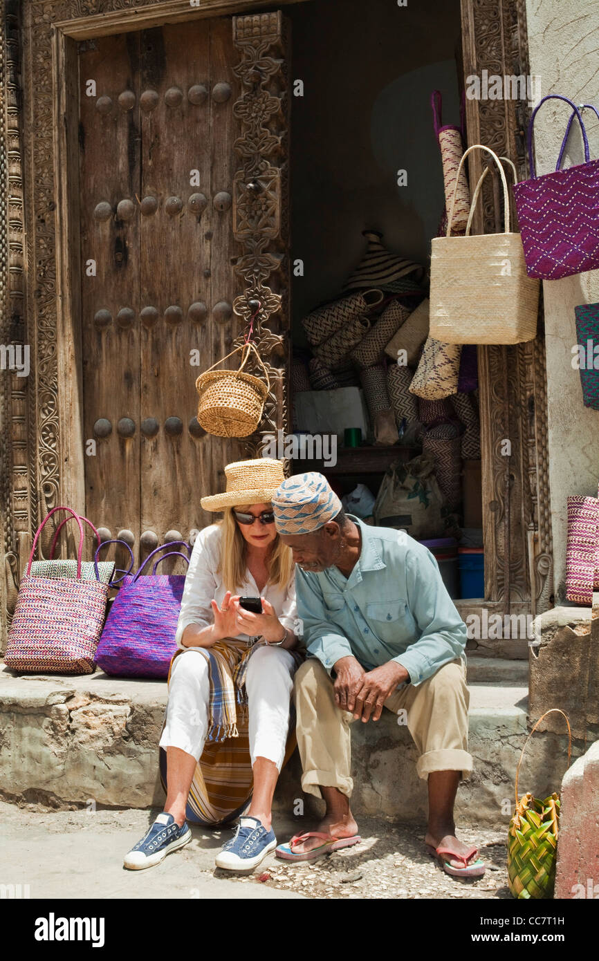 Tanzania, Zanzibar, Stone Town. An enterprising hat maker with an  eye-catching display on the wall of the old Omani Fort bargains with a  passing tourist. - SuperStock