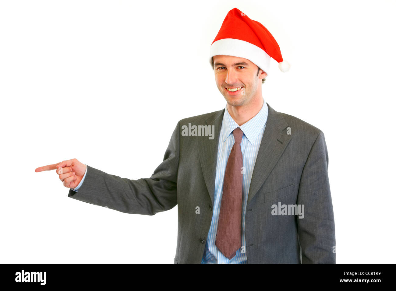 Smiling young businessman in Santa hat pointing finger at copy space ...