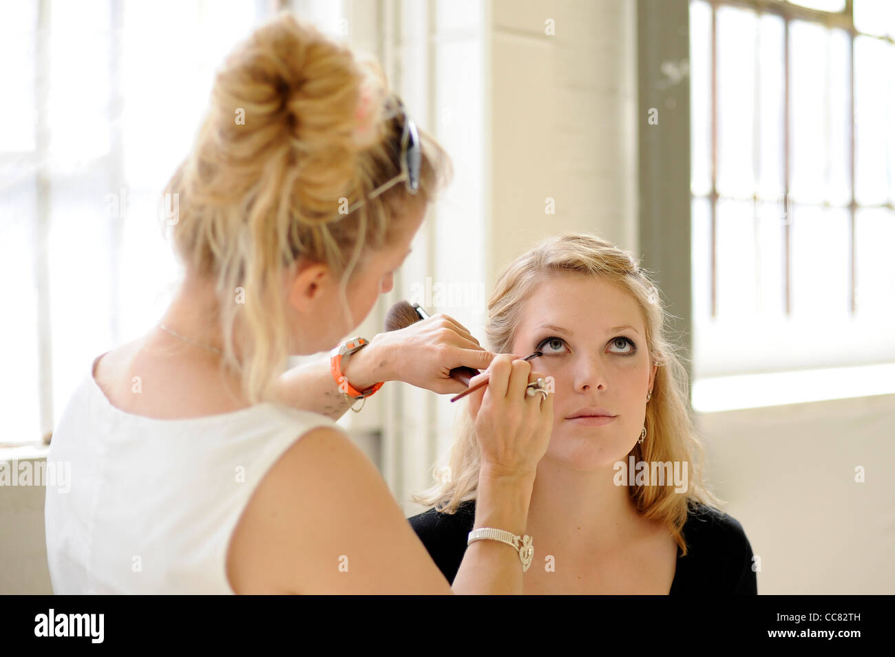 A young blonde model has make up applied for a fashion shoot in a naturally lit studio - Image Copyright Ben Pruchnie 2011 Stock Photo