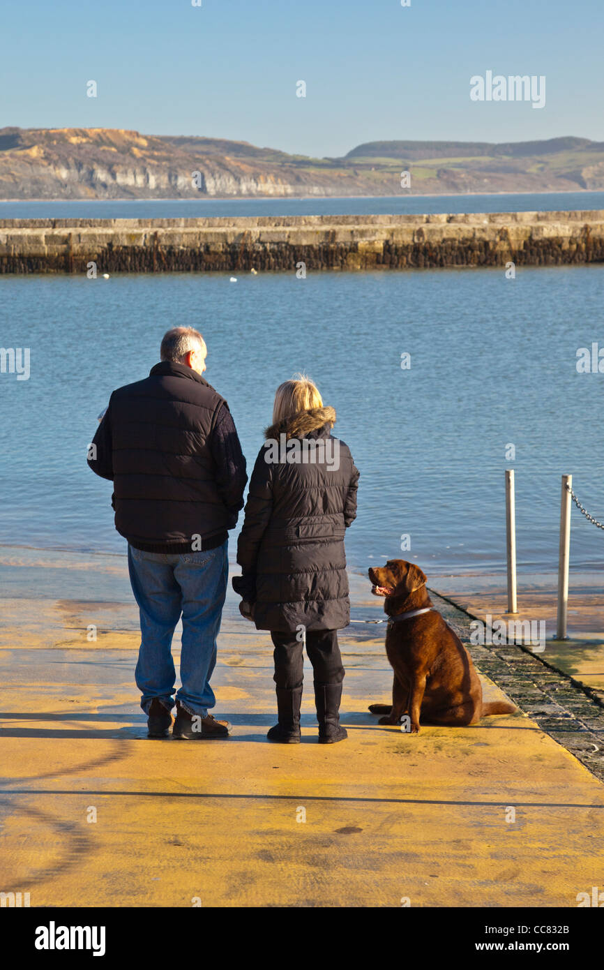 Two pet owners and their dog at the harbour in Lyme Regis on a winter