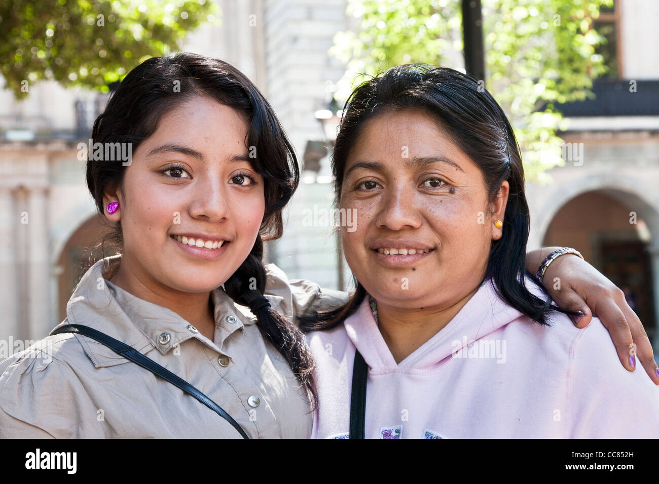 pretty smiling bright eyed Mexican teenager poses for affectionate street portrait with her mother in Oaxaca Zocalo Mexico Stock Photo