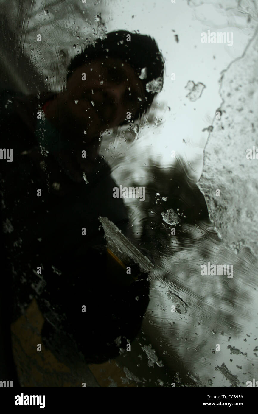 view from the inside of a car as a man scrapes ice off the windshield Stock Photo