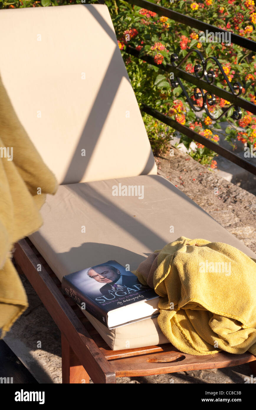A towell and a book to reserve a sun lounger beside a hotel swimming pool Stock Photo