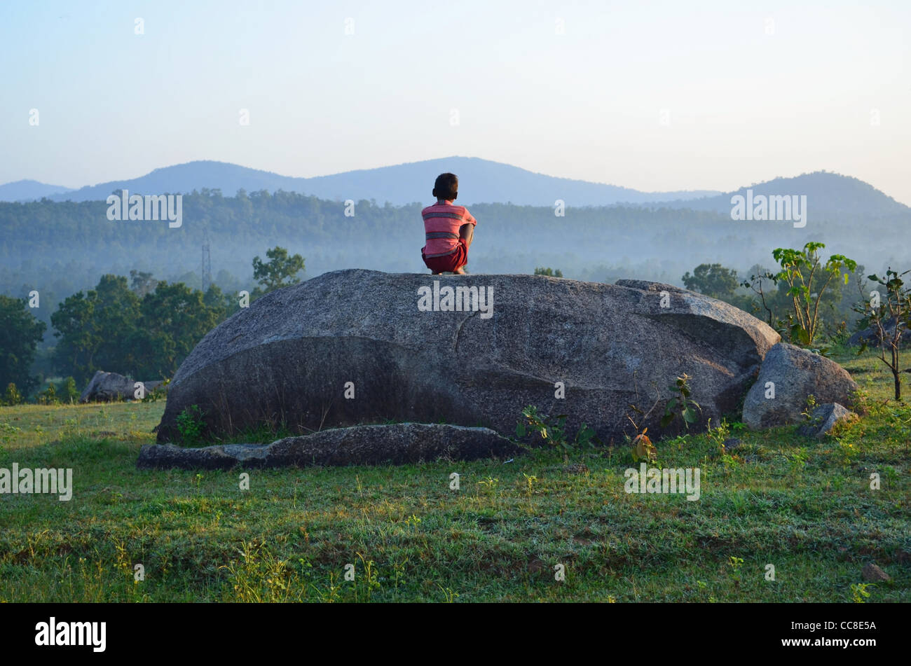 Boy sitting on a large rock and watching the scenic view Stock Photo ...