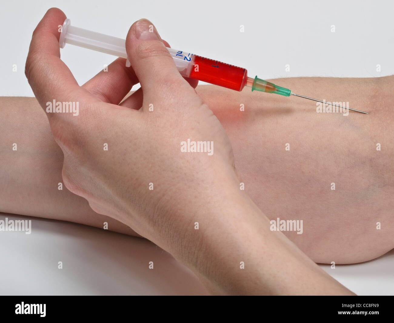 eine Spritze mit roter Flüssigkeit wird in den Arm gespritzt | a syringe with red liquid is injected into the arm Stock Photo