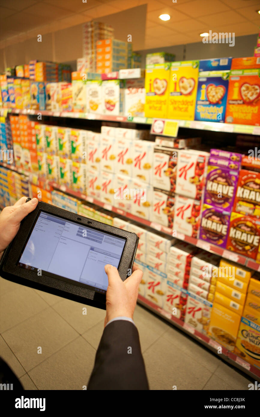 Handheld tablet at a supermarket shelf for order taking of cereals held by man in suit showing arms only Stock Photo