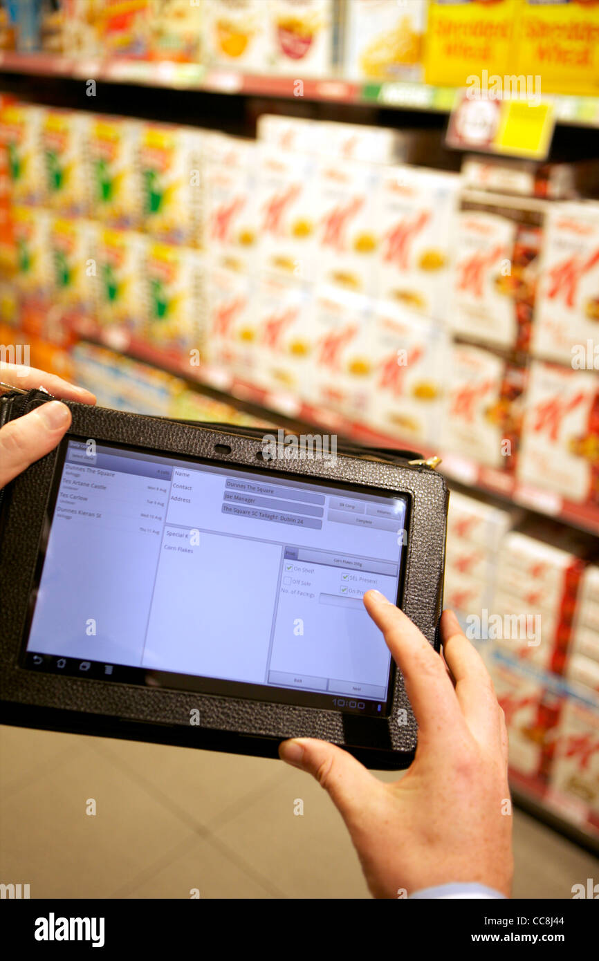 Handheld tablet at a supermarket shelf for order taking of cereals held by man in suit showing arms only Stock Photo