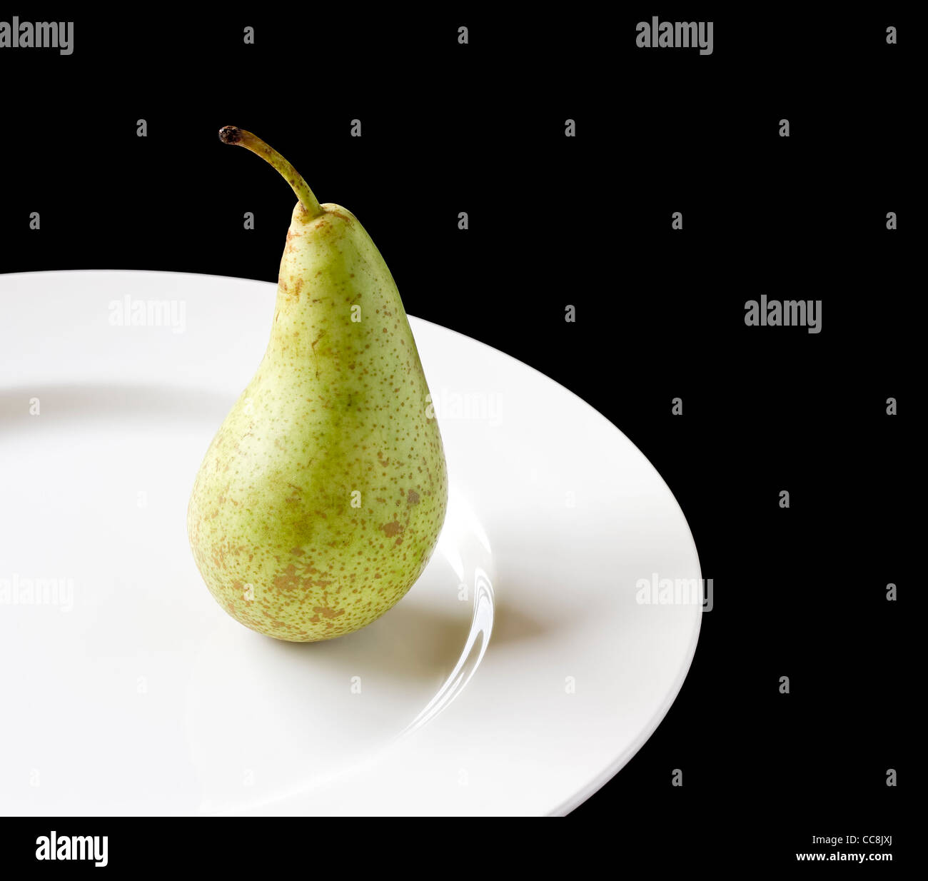 Ripe juicy pear on white plate with black background Stock Photo