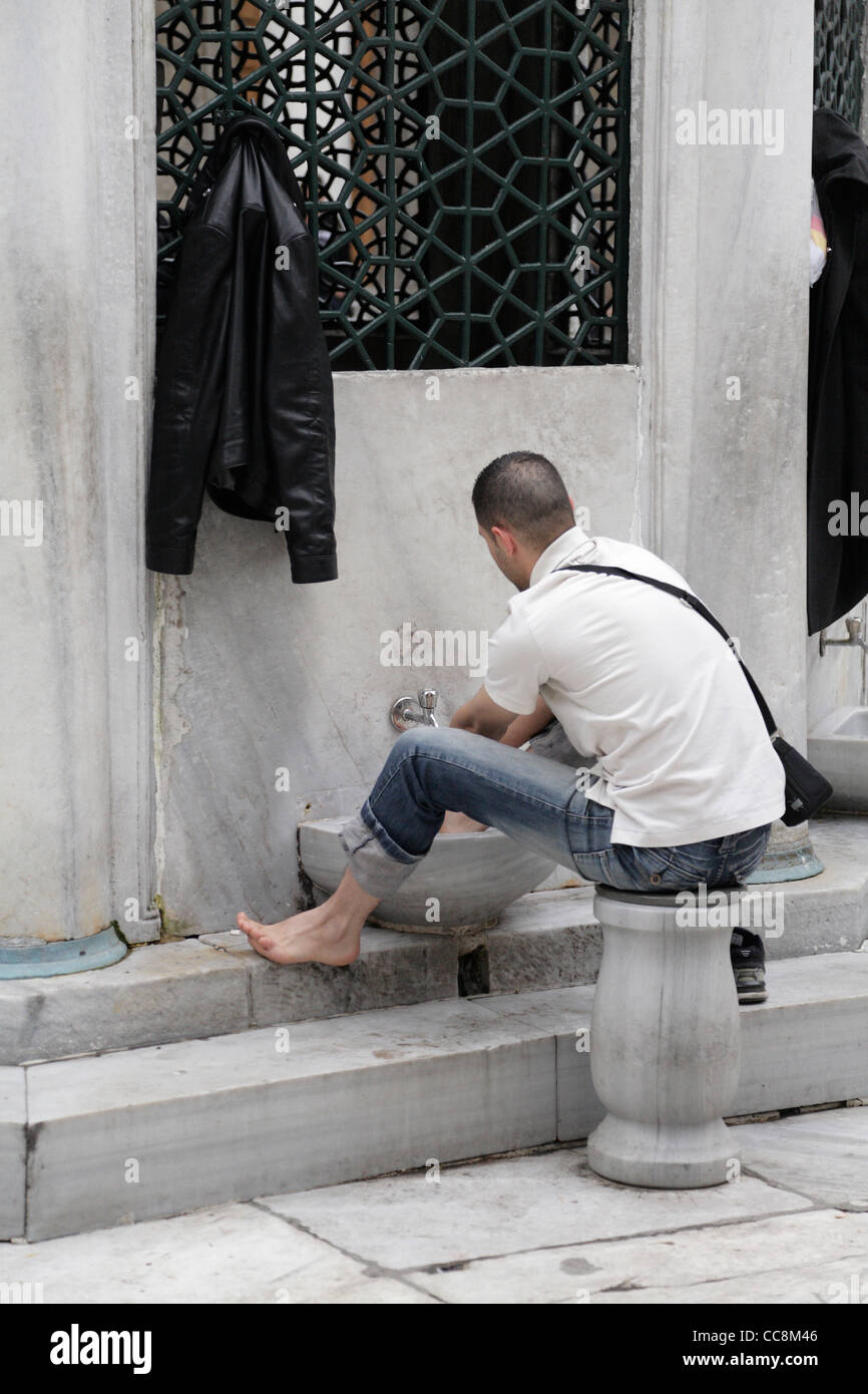 Young muslim man washing his feet at mosque wudu The New Mosque Yeni Cami. Ritual washing prior to prayer islam islamic law Stock Photo