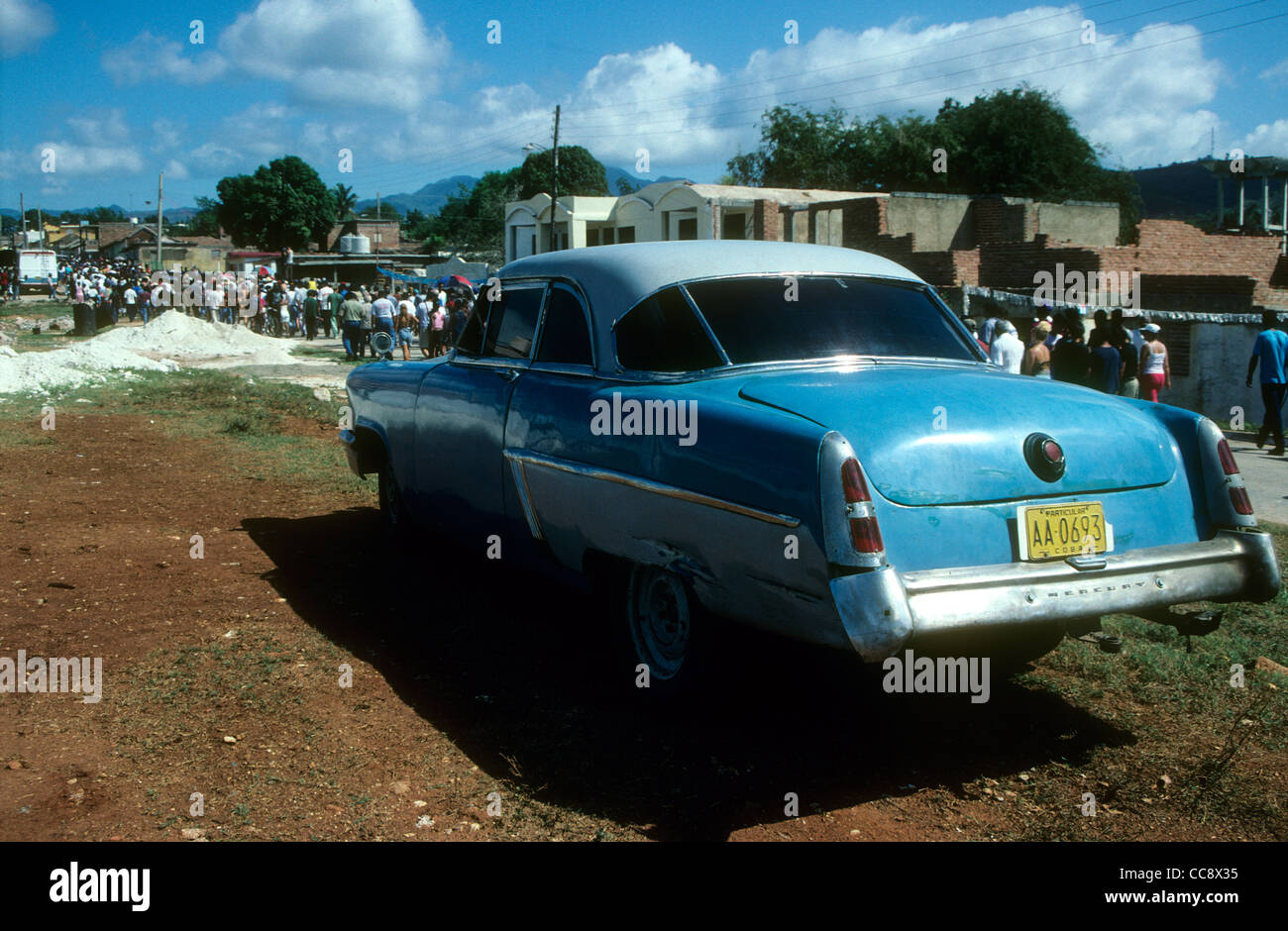 An old American car parked beside a dirt road in Trinidad, Cuba. The people in the background are returning from a May Day Rally Stock Photo