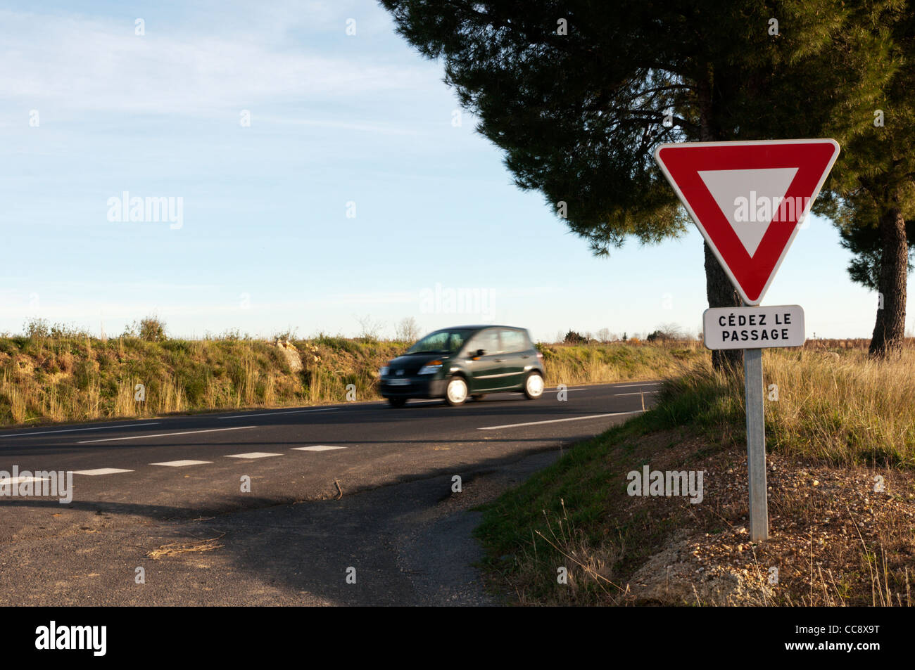 A car, motion blurred, passing a French road sign warning drivers to give way when joining a main road. Stock Photo