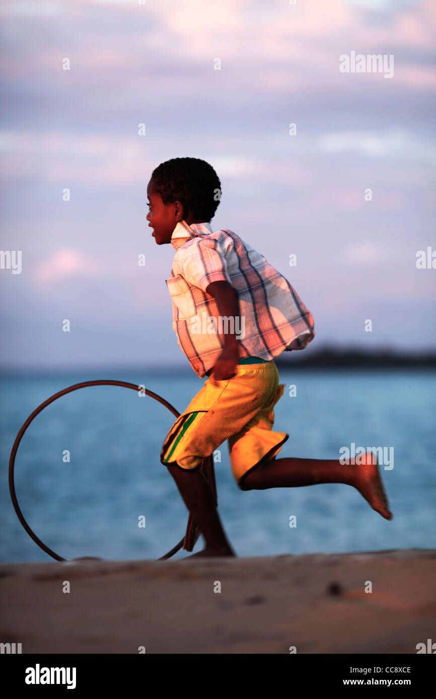 A local young malagasy african boy 6-10 years running with a stick and a bicycle rim, a traditional toy. Nosy Komba, Madagascar Stock Photo