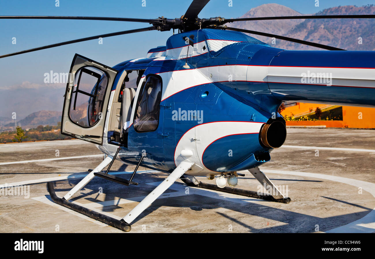 Blue and white helicopter on a landing spot at a helipad landscape with Trikuta mountain range as a backdrop Stock Photo