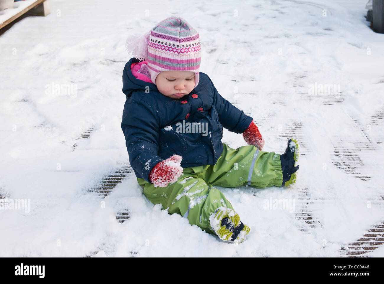 Baby Girl wearing Snow Suit sitting on Ground in Snow Stock Photo