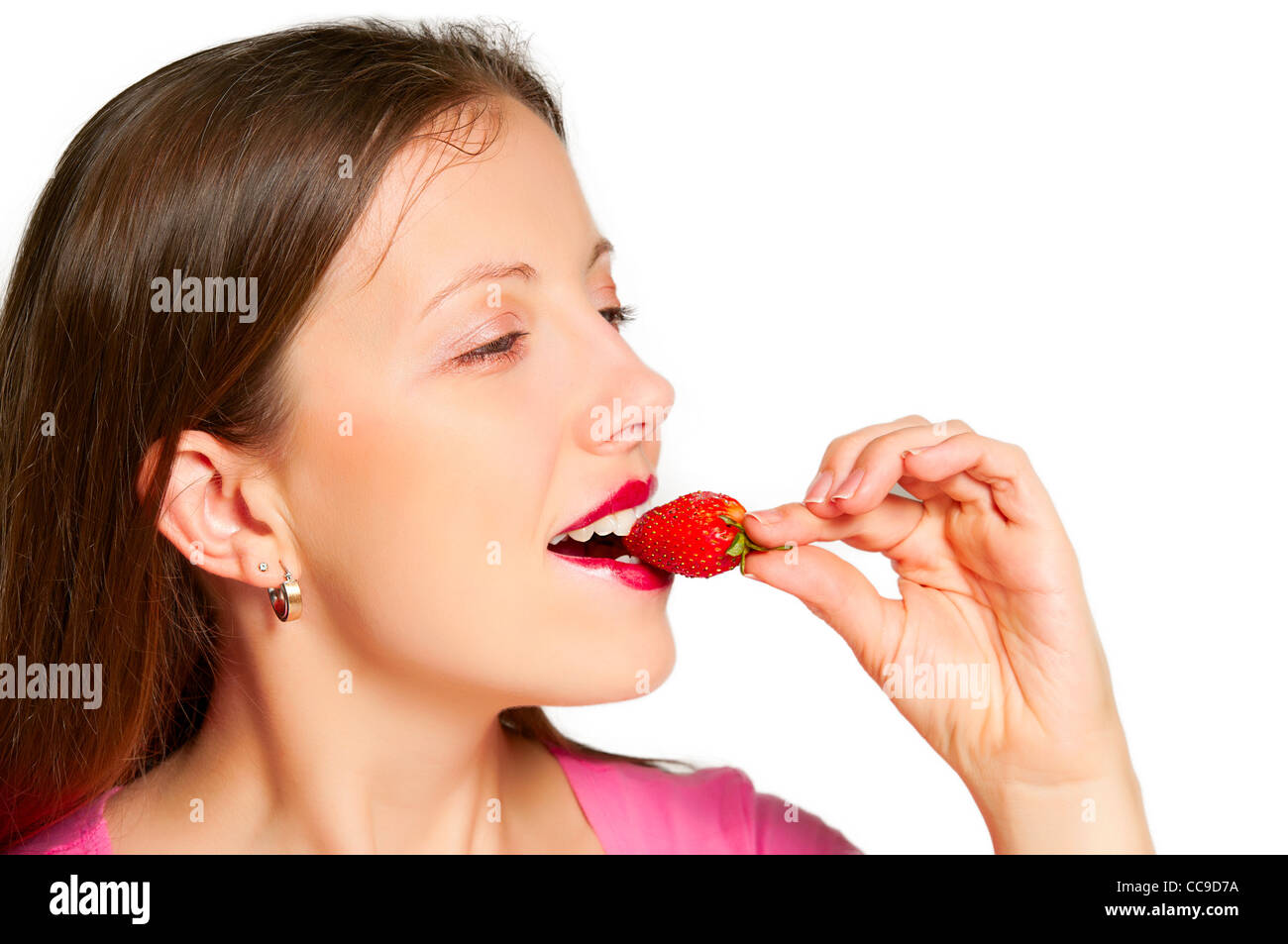 Beautiful girl takes a bite out a piece of strawberry keeps her leaves Stock Photo