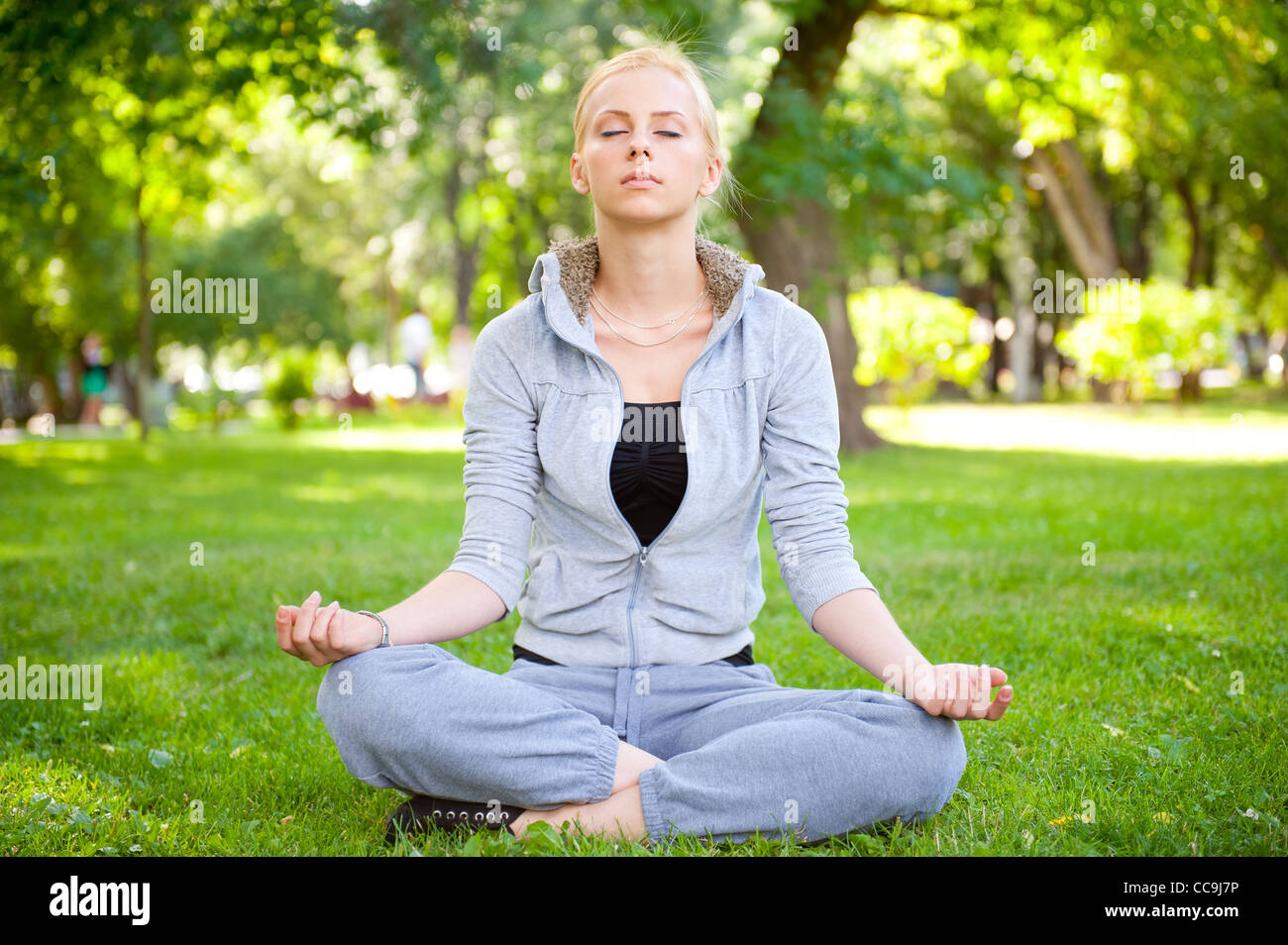 Portrait of young woman meditating in pose of lotus on green grass on ...