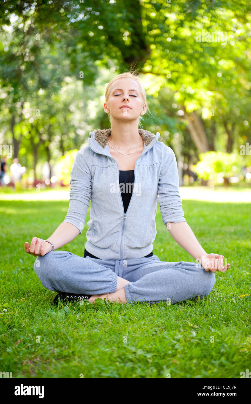 Portrait of young woman meditating in pose of lotus on green grass on ...