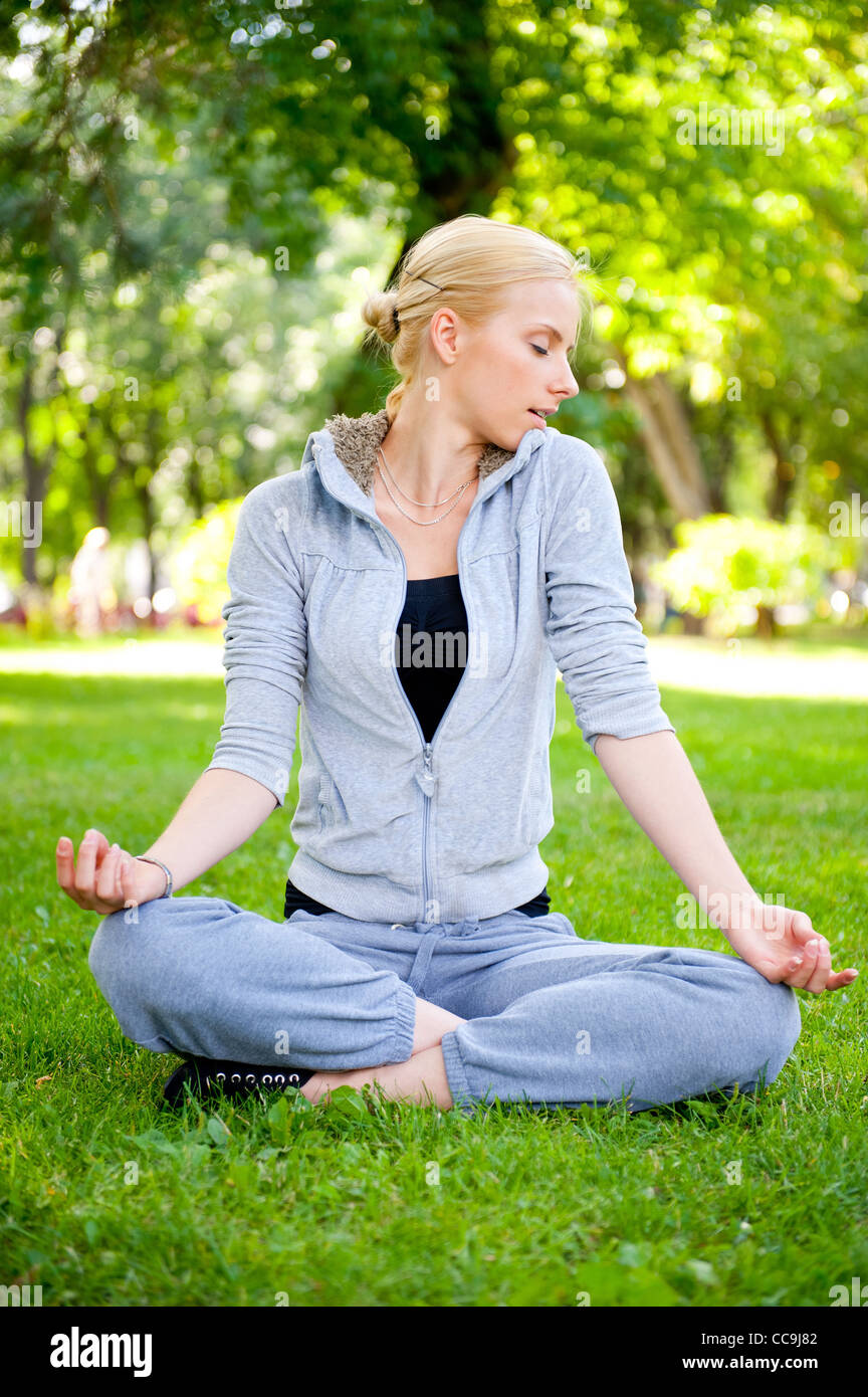 Portrait of young woman meditating in pose of lotus on green grass on ...