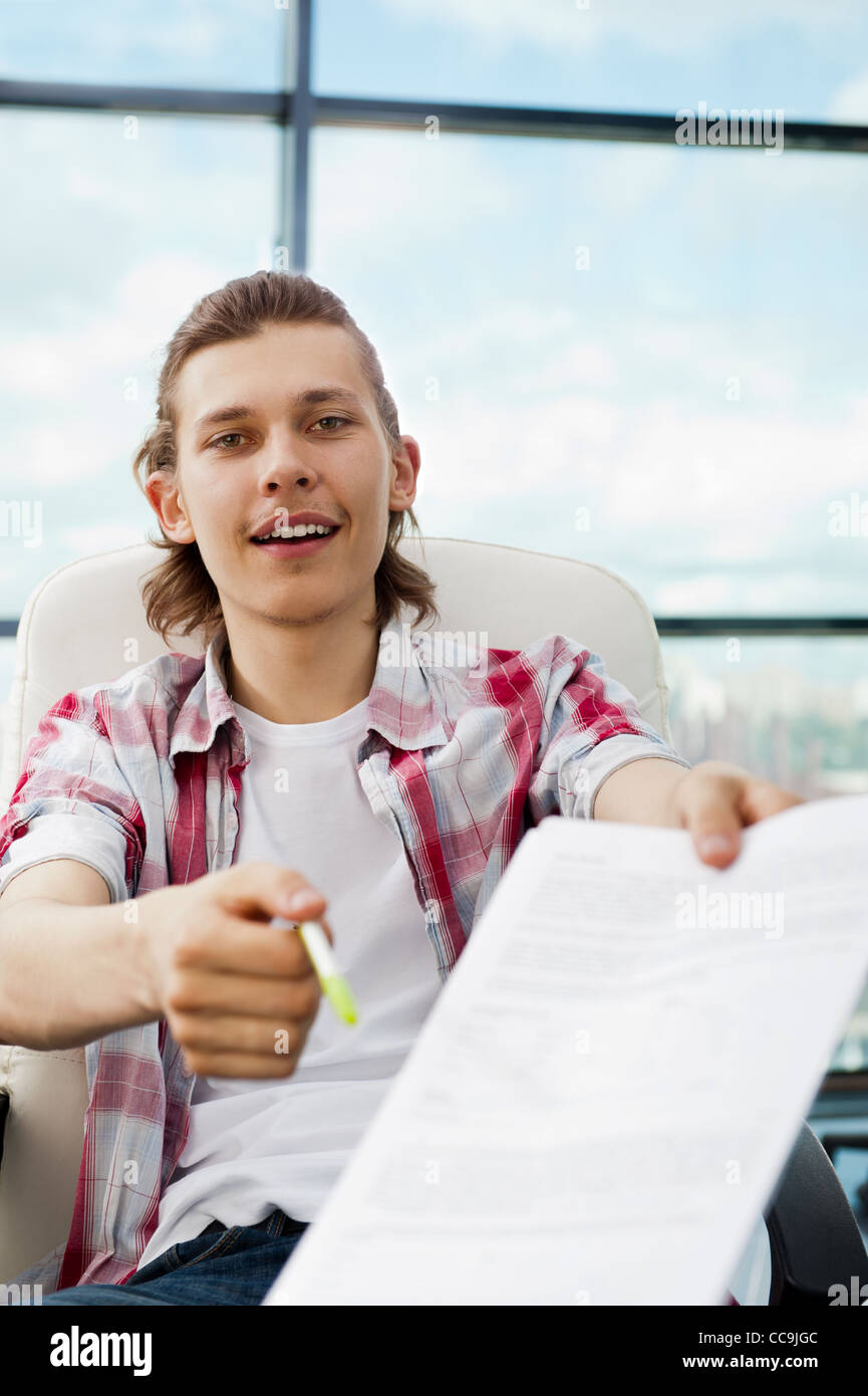 Portrait of a happy young freelancer giving pen and blank agreement to camera for signing Stock Photo