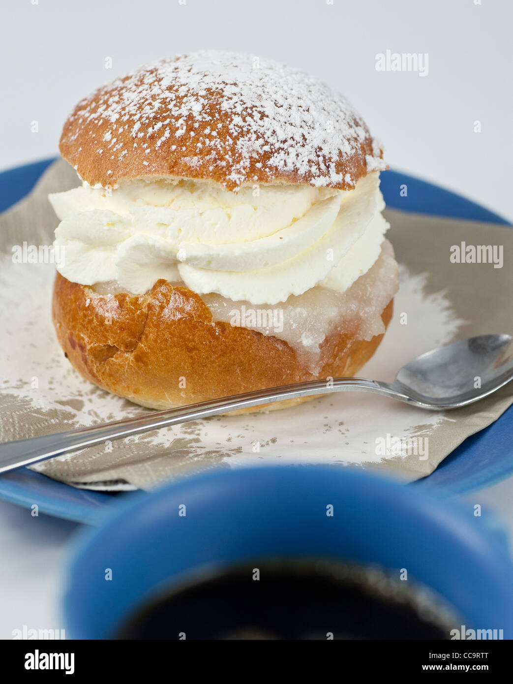 Cream bun with almond paste on a plate with a cup of coffe in front Stock Photo