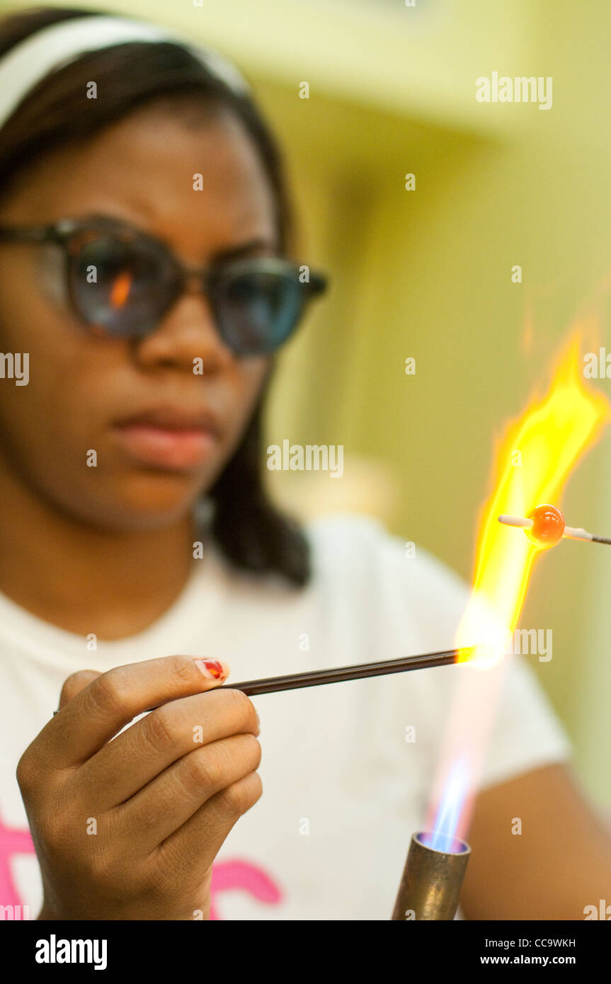 a teenage girl melts glass over a flame to make a jewelry bead for a