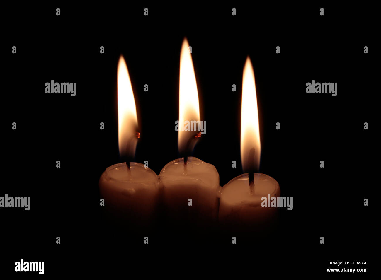 three candles burning, two of them with glowing wick, on black