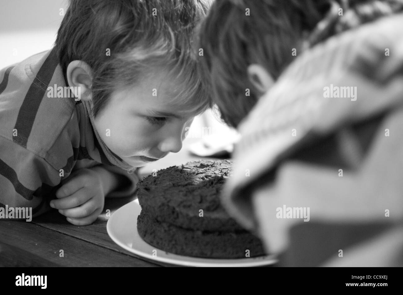 Young happy boy sitting at the table eating a piece of chocolate sponge cake Stock Photo