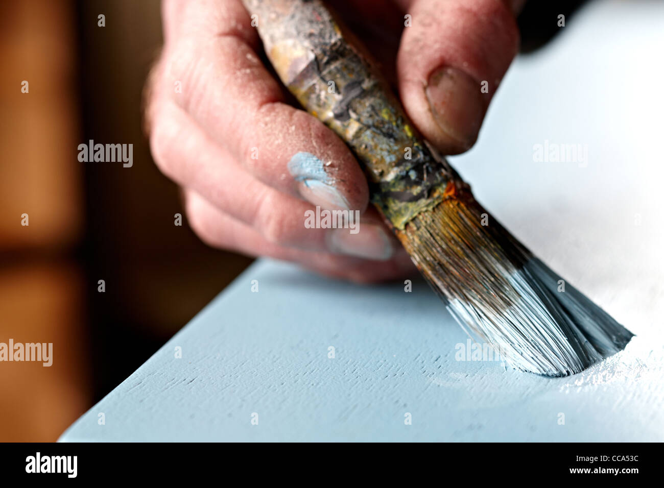A craftsman paints a door using a paintbrush and blue paint Stock Photo