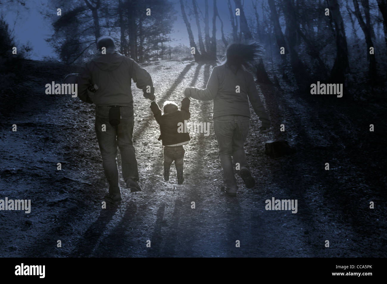 Young family playing swinging young boy while holding hands and walking in the forest Stock Photo