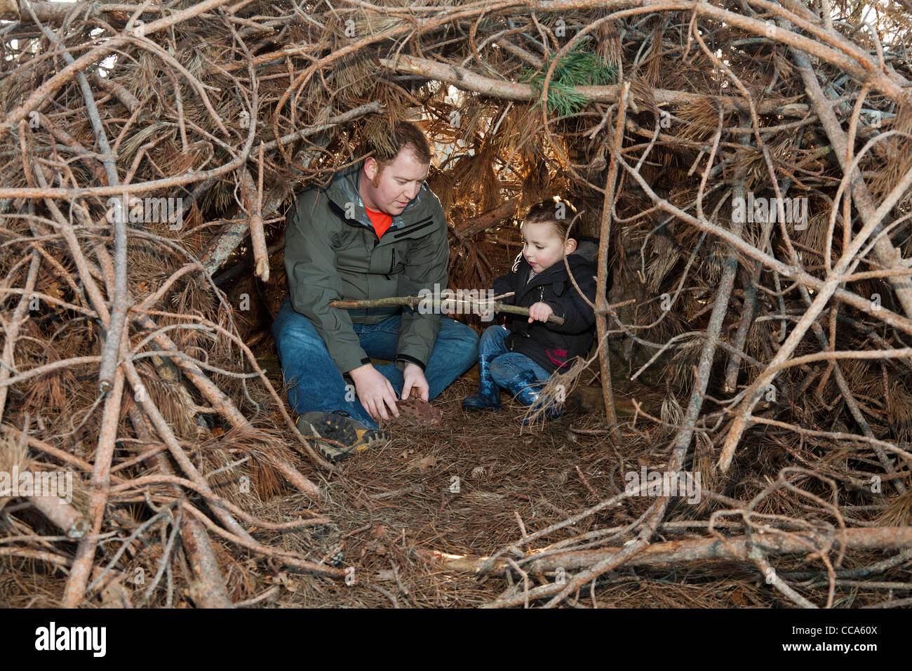 Father and son playing together in a hide-away camp den made from branches, sticks and wood from the forest Stock Photo