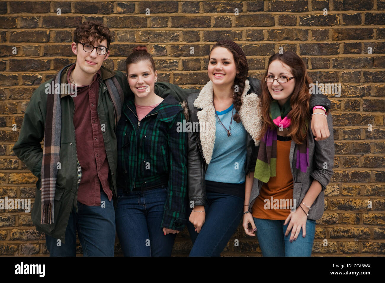 Four young friends against brick wall, smiling Stock Photo