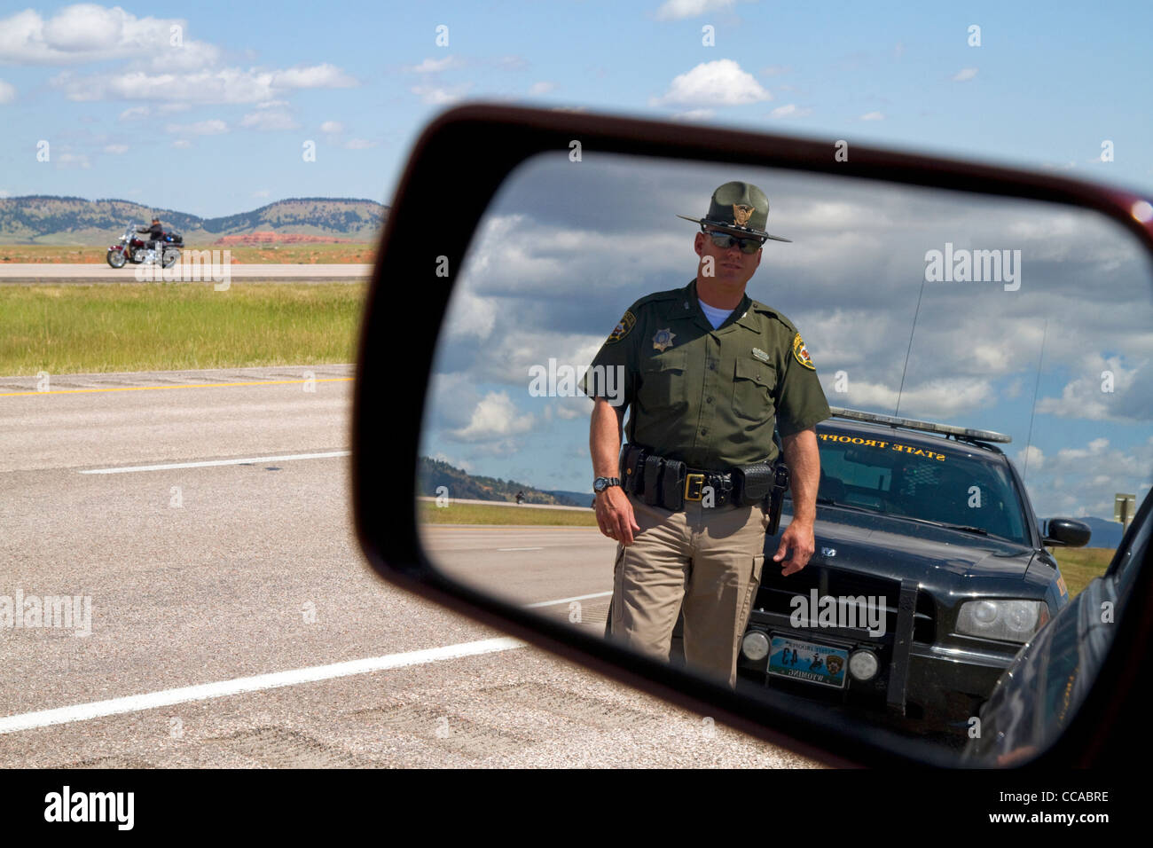 Wyoming Highway Patrol officer on seen in rear-view mirror along I-90 near the Wyoming, South Dakota border, USA. MR Stock Photo