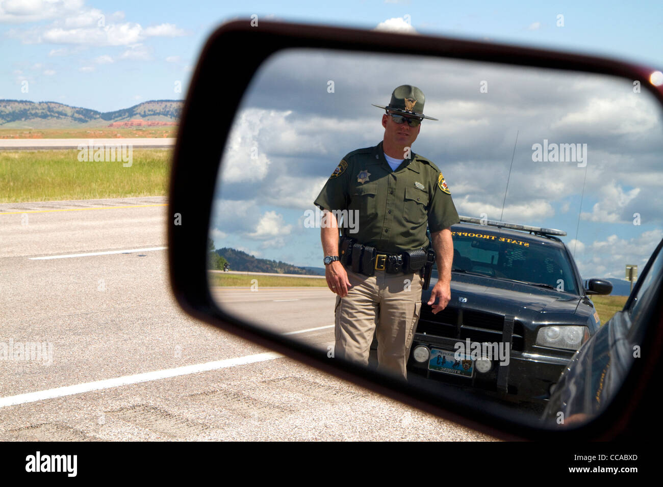 Wyoming Highway Patrol officer on seen in rear-view mirror along I-90 near the Wyoming, South Dakota border, USA. MR Stock Photo