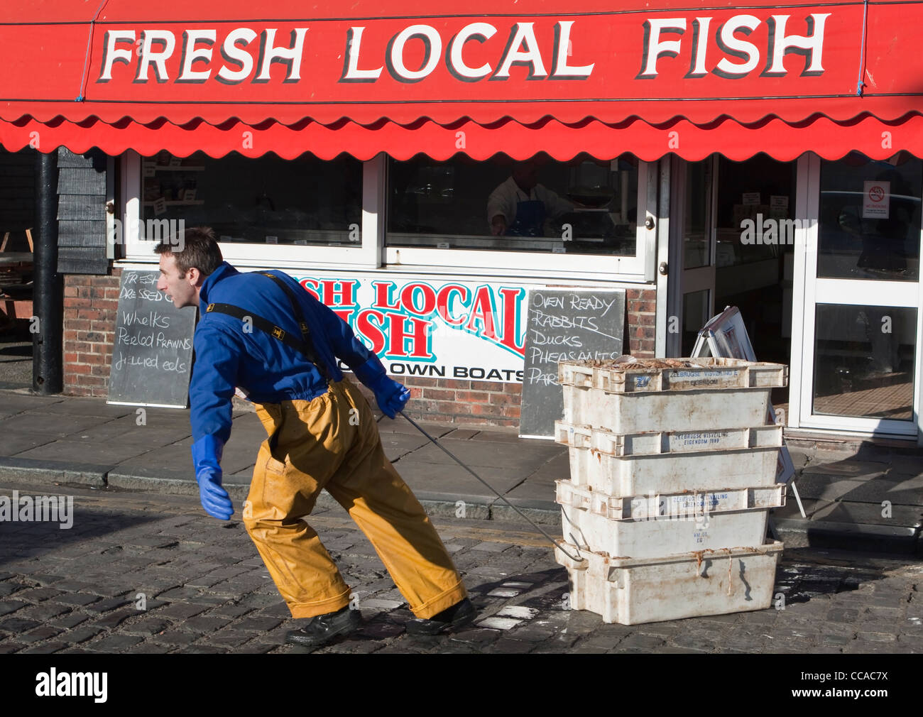 Fisherman Pulling Crates of Fish in front of a Fresh Fish Shop in Folkestone Kent Stock Photo