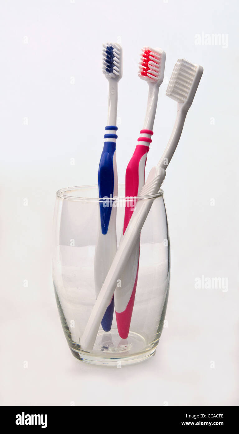 three toothbrushes in a glass, pink blue and white. Stock Photo