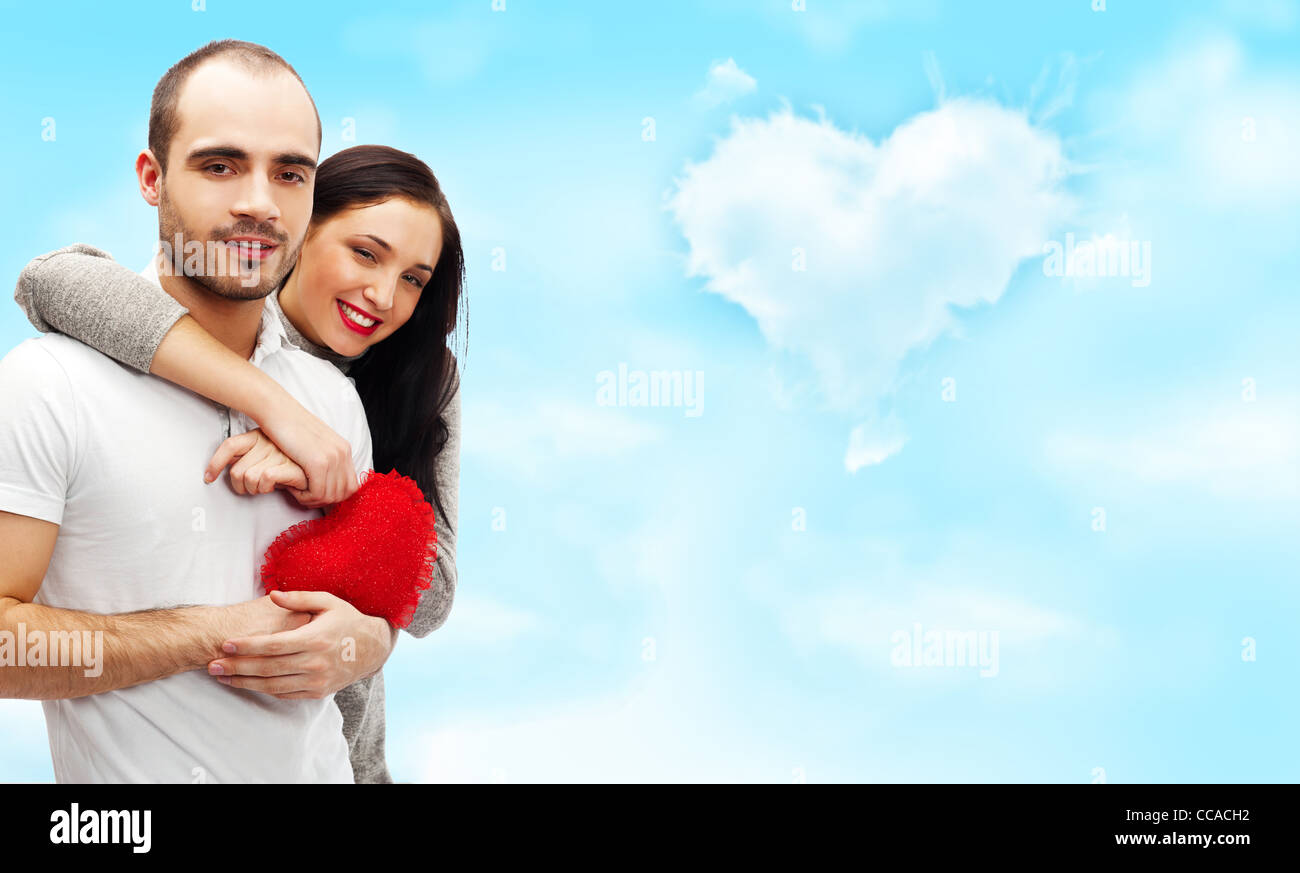 Happy young adult couple with red heart on romantic background with sky ...