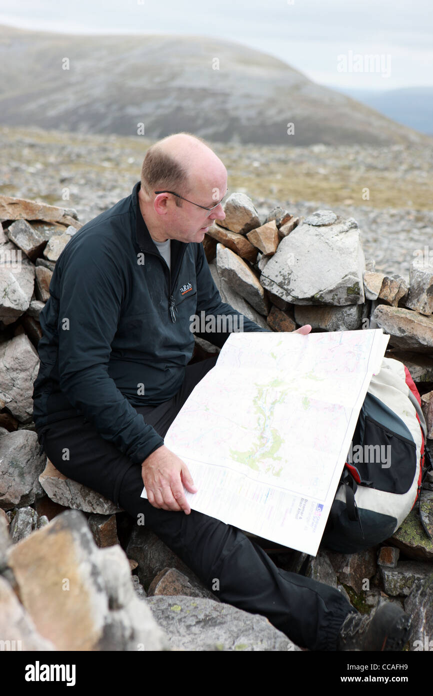 Walker reading an OS map in a summit cairn of one of the Cairngorm mountains Stock Photo