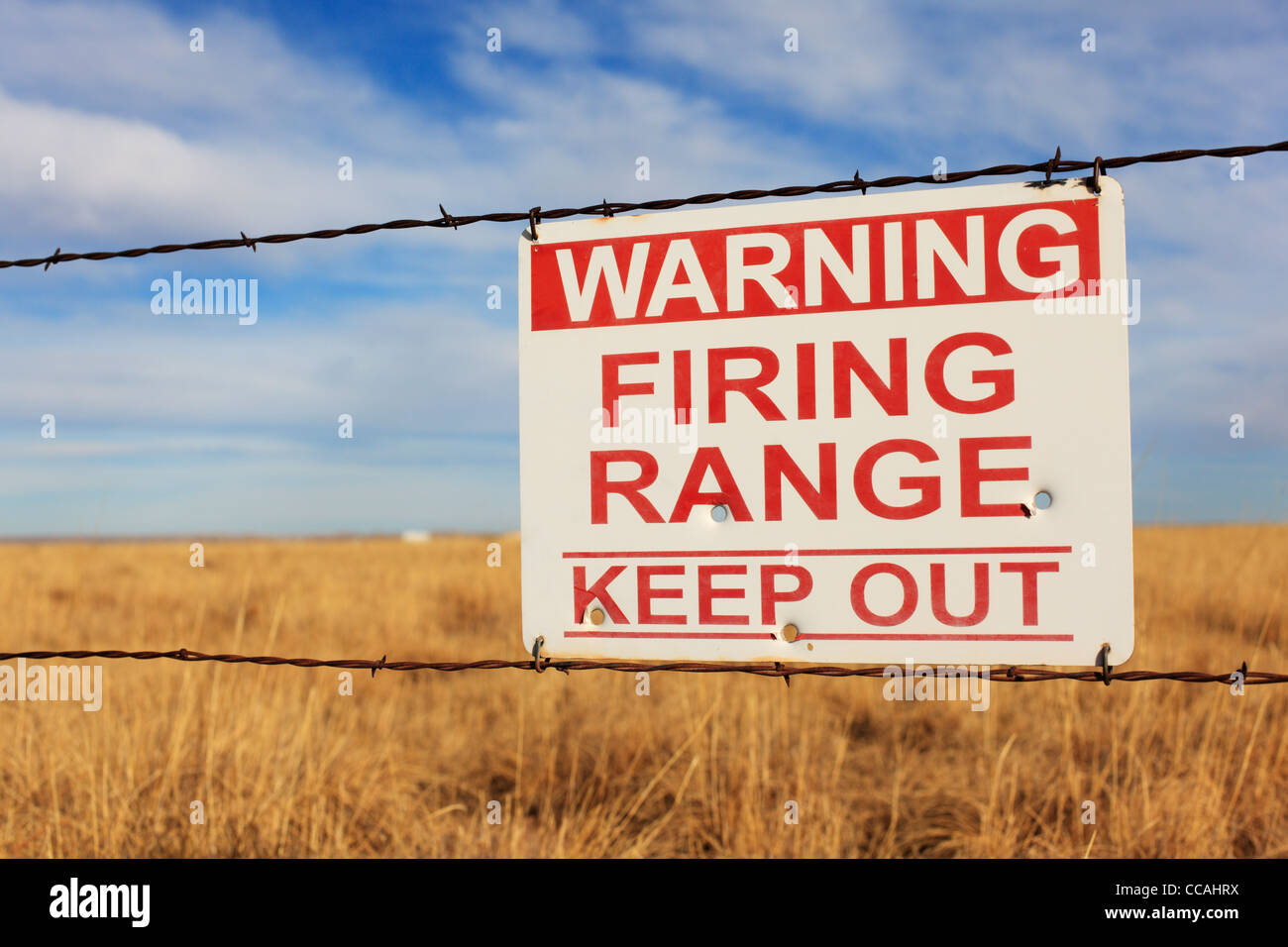 Warning Firing Range Keep Out sign hanging on a barbed wire fence. Stock Photo