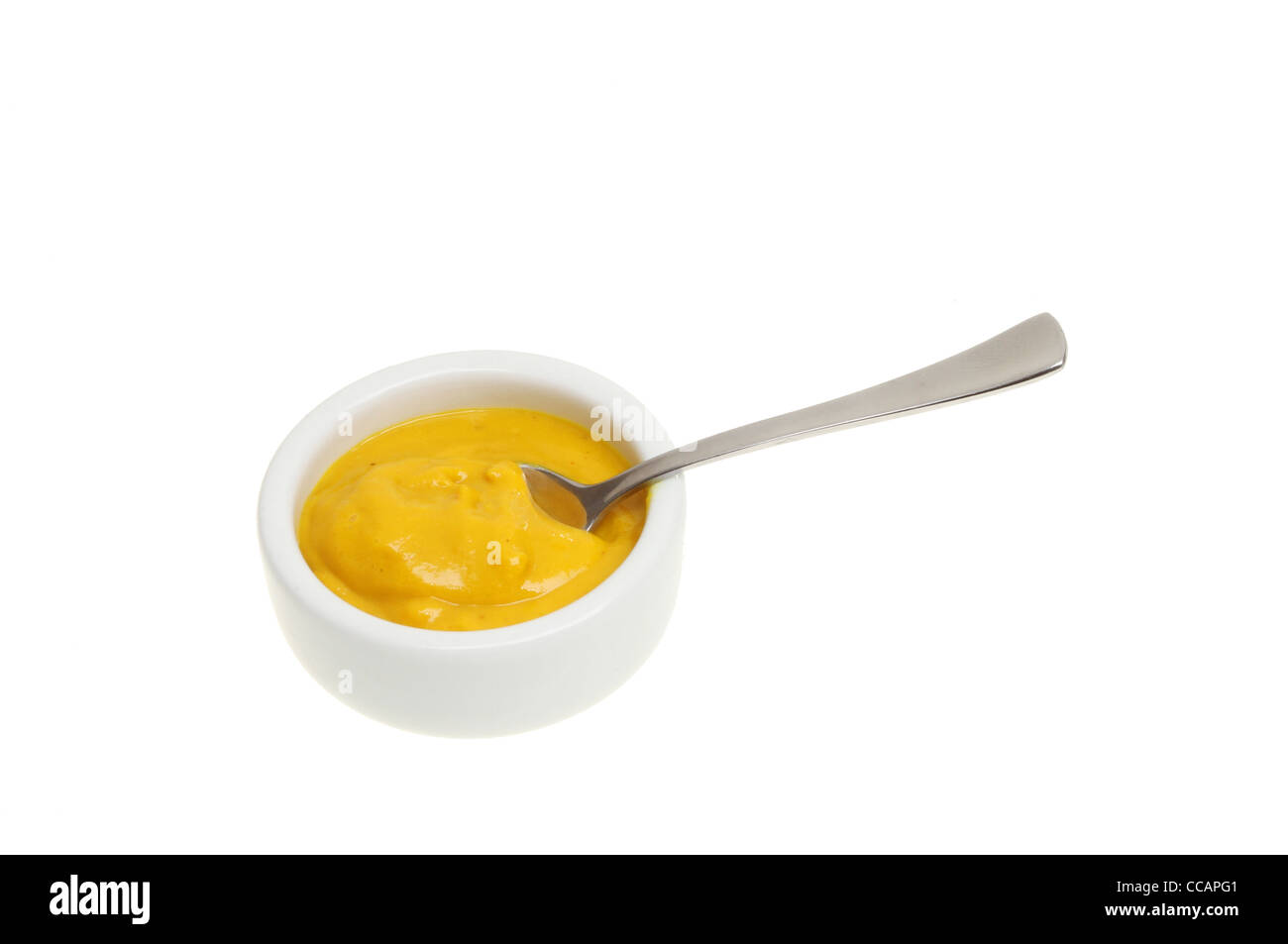 English mustard in a ramekin with a spoon isolated against white Stock Photo